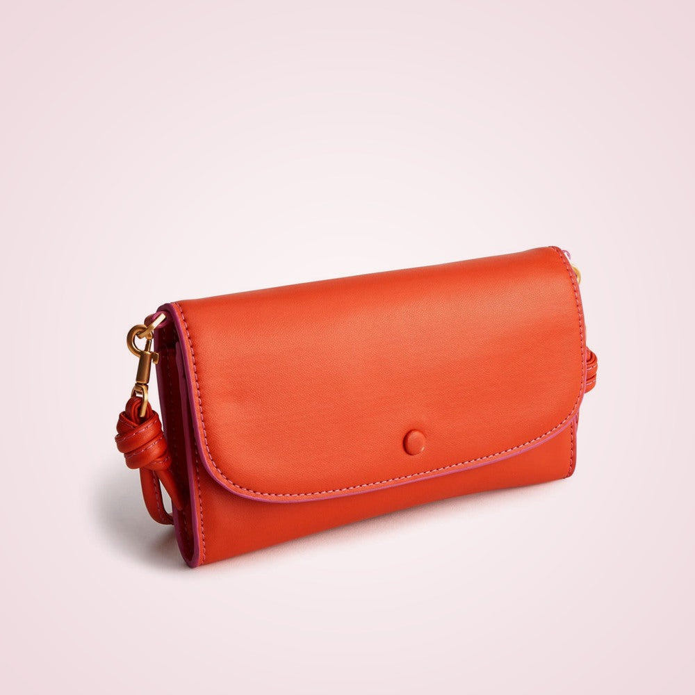 Orange bonded leather flap clutch wallet on a soft rose background